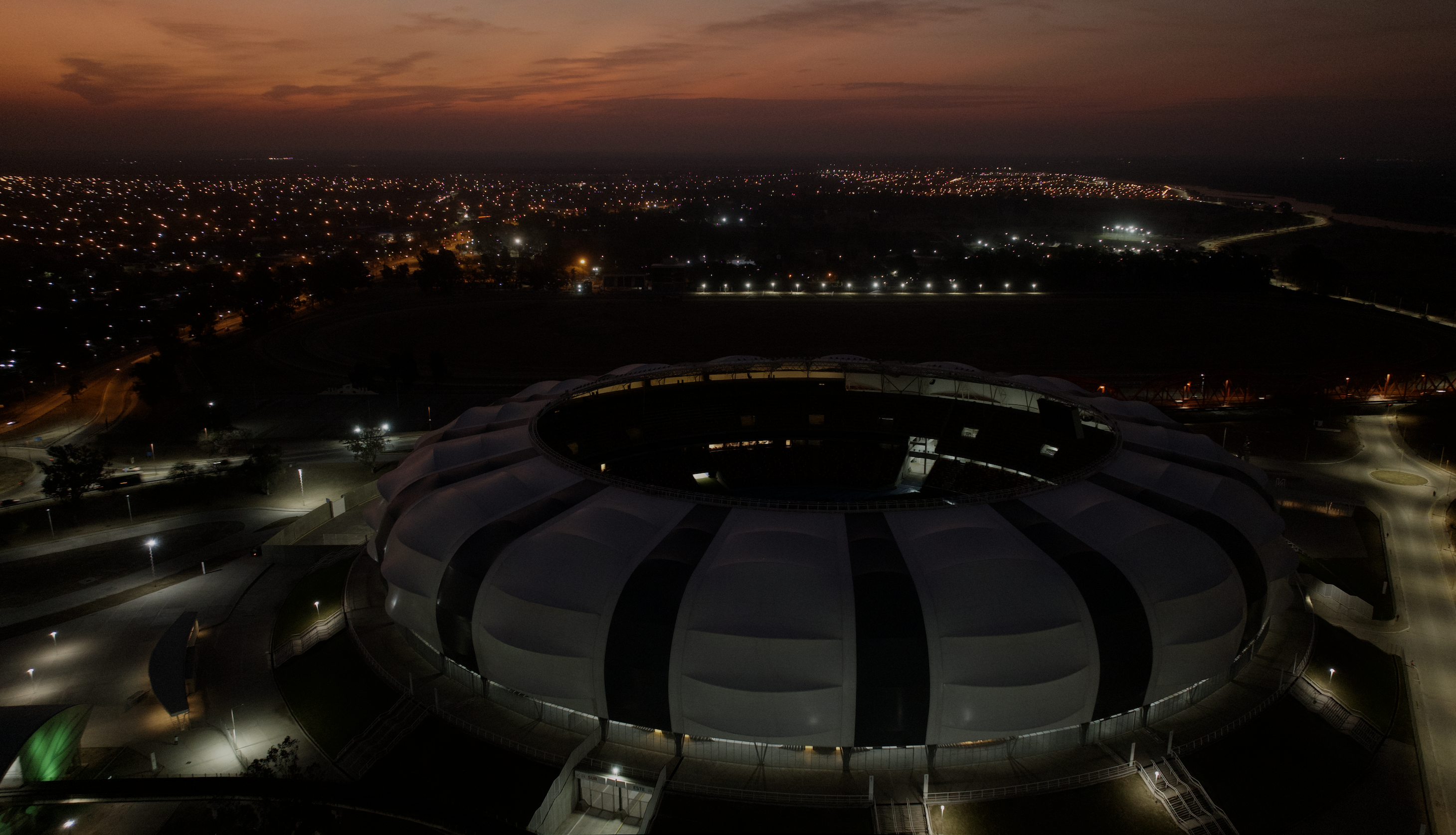 Vista aérea nocturna de un estadio iluminado y su entorno urbano.