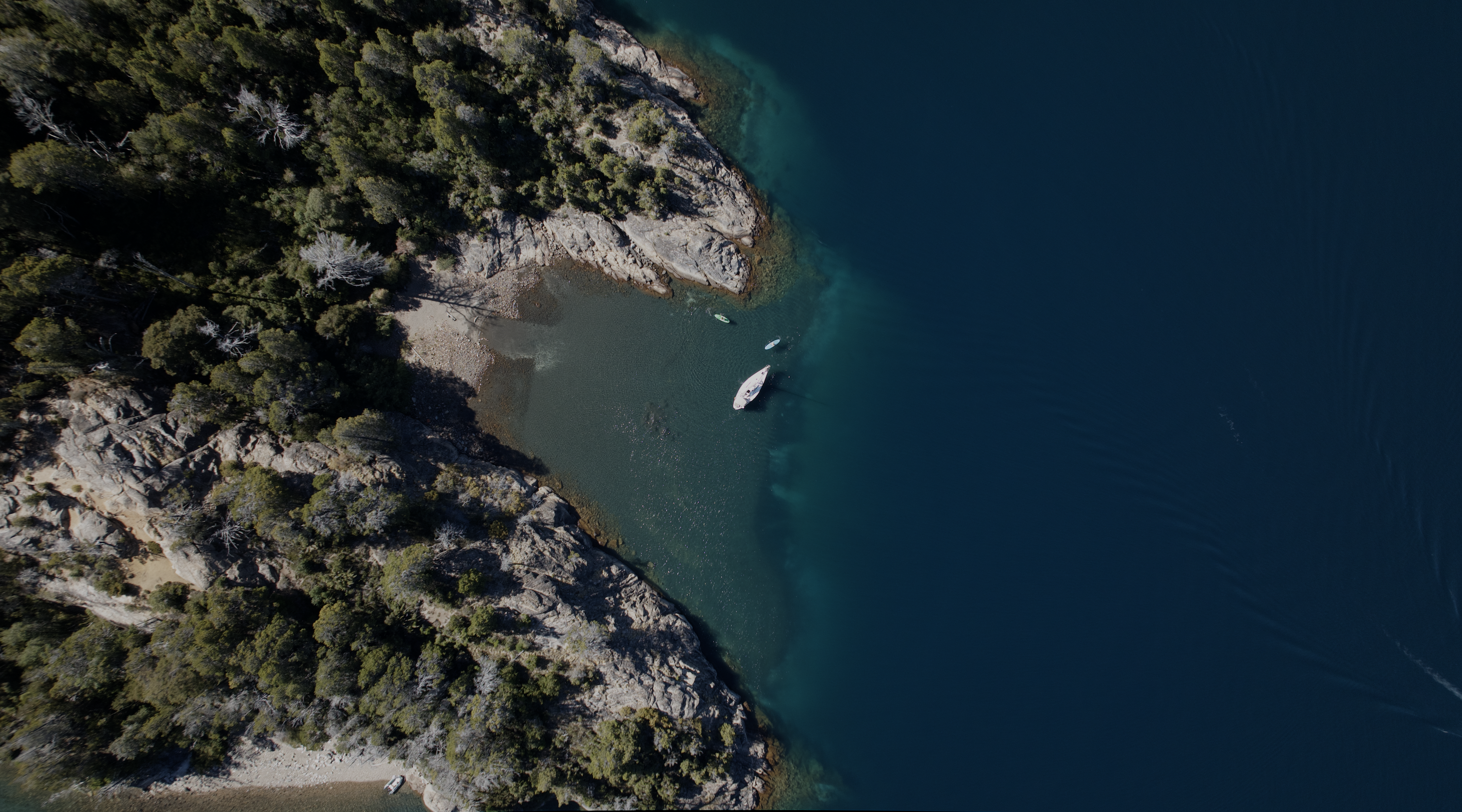 Vista aérea de una costa rocosa con una embarcación navegando junto a aguas profundas.